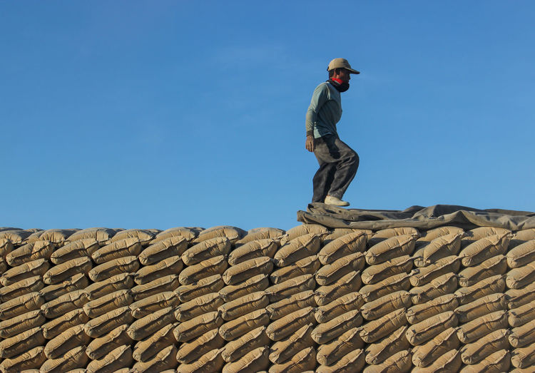 Low angle view of man standing on rooftop against blue sky
