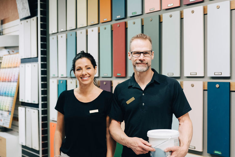 Portrait of smiling coworkers standing against multi colored wall in store