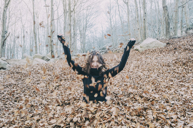 Woman enjoying autumn and catching falling yellow leaves