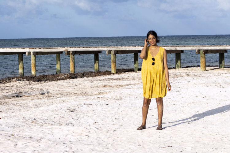 Full length of smiling woman standing at beach