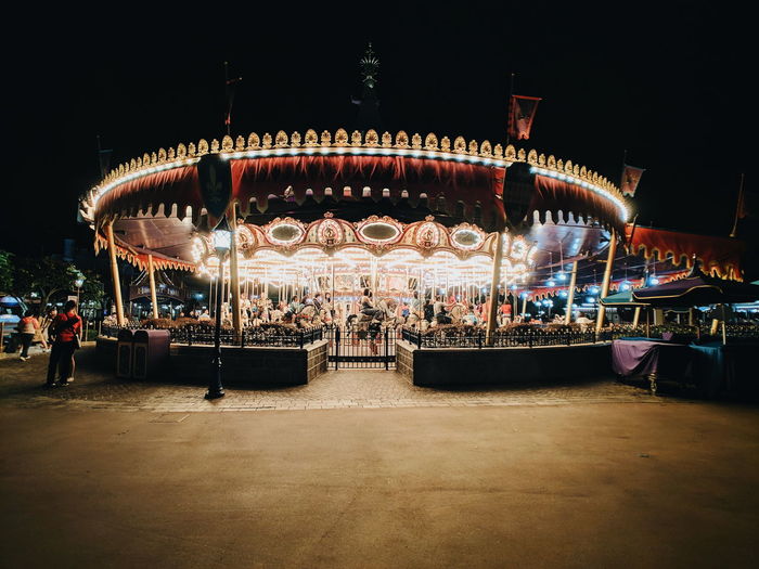 Illuminated carousel at amusement park against sky at night