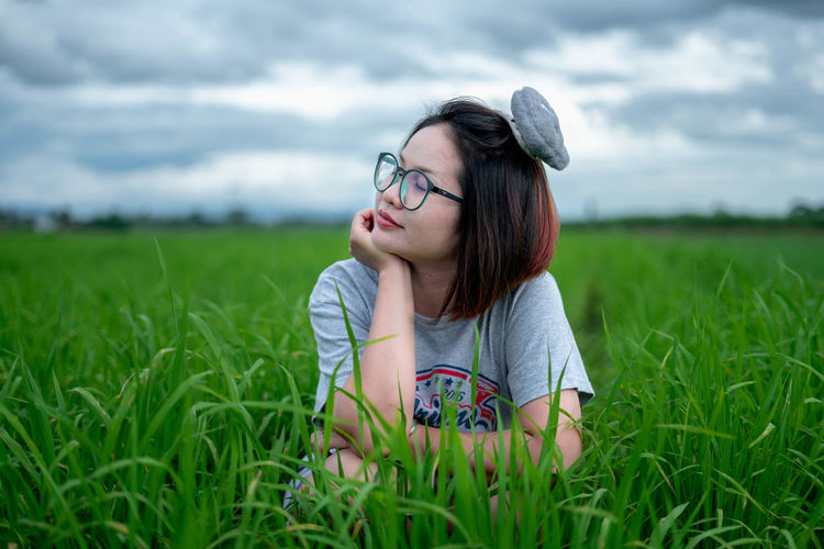 Woman wearing eyeglasses crouching on field against sky