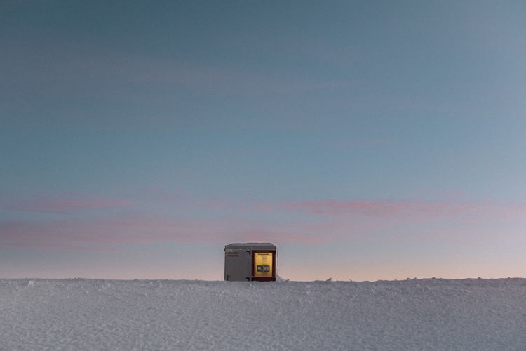 Built structure on snow covered land against sky during sunset