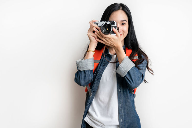 Portrait of young woman photographing against white background