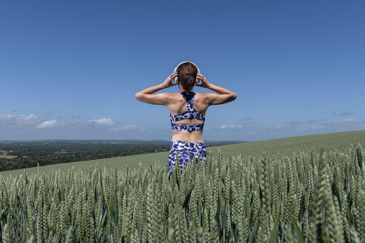Sporty, fit woman listening to music with wireless headphones in a field.rear view