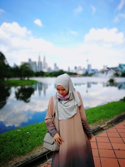 Muslim woman looking down while standing on footpath against sky
