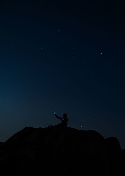 Low angle view of man standing on mountain against sky at night