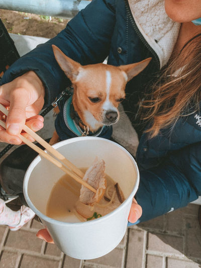 Midsection of woman holding dog and eating ramen