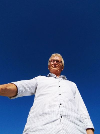 Low angle view of smiling senior man standing against clear blue sky