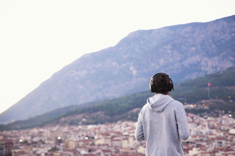 Rear view of woman wearing headphones against mountains