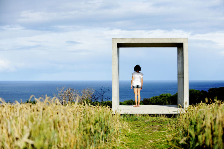 Girl standing in concrete square and looking at sea