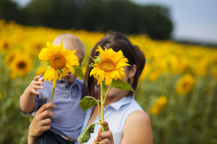 Mother with son holding sunflowers while standing amidst plants