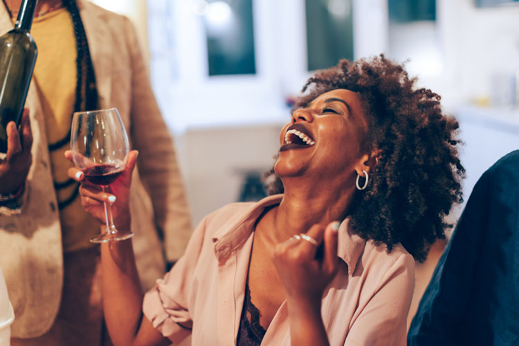African american woman laughing at party - young female person holding glass of wine at dinner