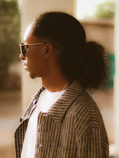 Side view of young man looking away while standing outdoors