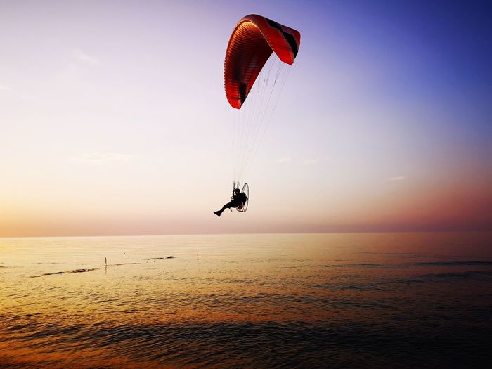 Silhouette person paragliding over sea against sky during sunset