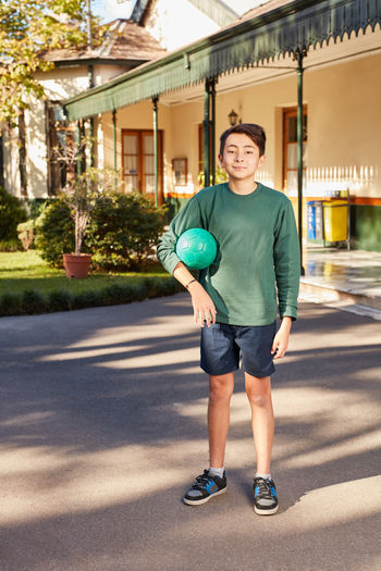 Portrait of smiling boy with ball standing at yard