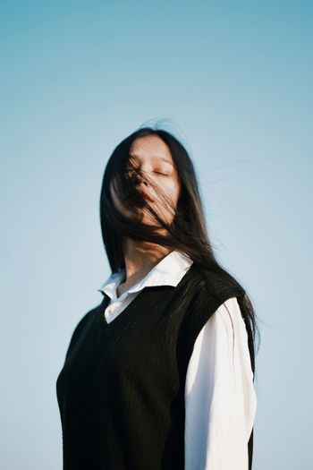 Low angle view of young woman standing against clear sky