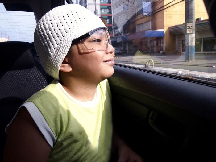 Close-up of boy wearing knit hat and eyeglasses looking through car window