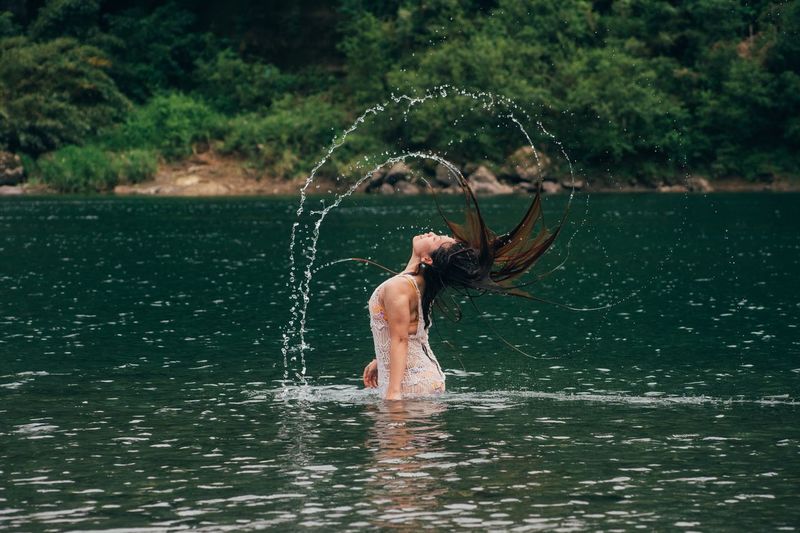 Side view of woman tossing wet hair in lake