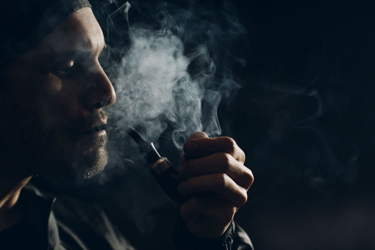 Man smoking pipe against black background