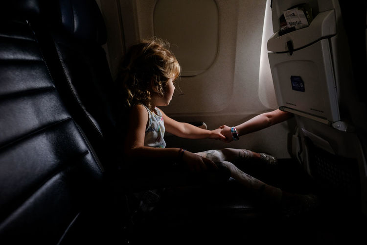 Little girl on airplane holding hands with sister in other aisle
