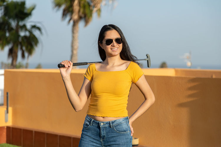Portrait of young woman wearing sunglasses while standing against yellow wall
