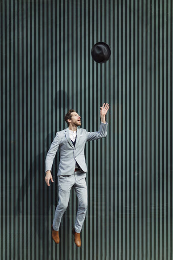 Businessman jumping while throwing hat against wall