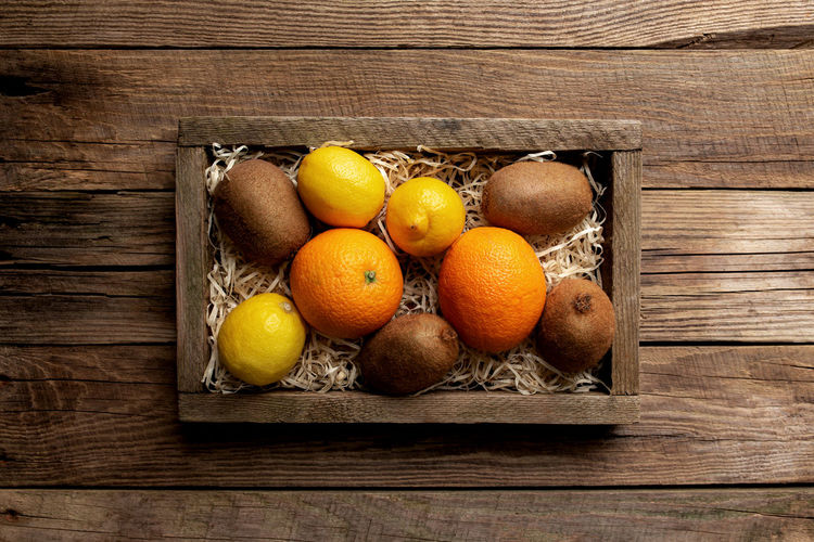 Fresh tropical fruits in a wooden delivery box on a wooden background. orange, kiwi, lemon top view