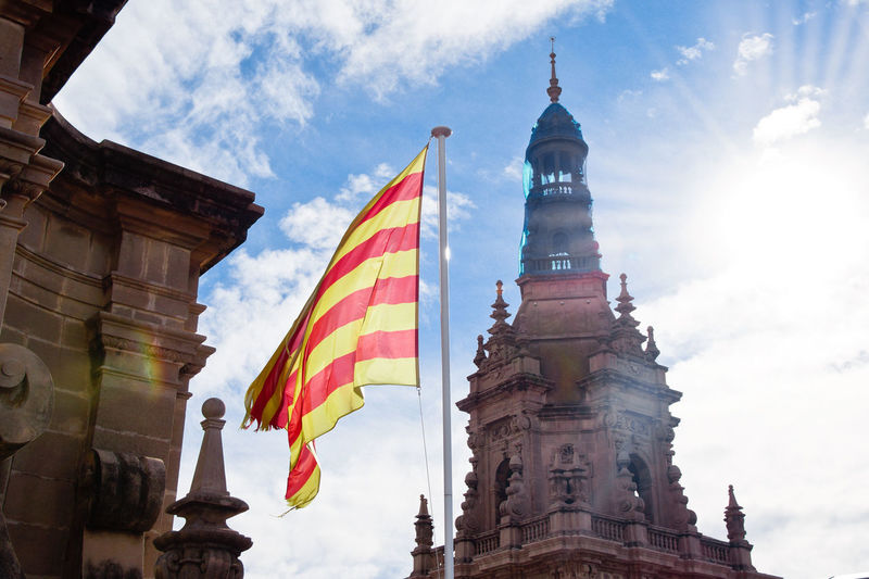 Low angle view of buildings and catalan flag against cloudy sky, barcelona, spain 