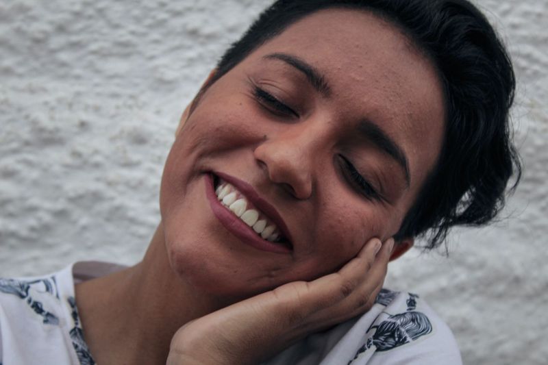 Smiling young woman with eyes closed against wall
