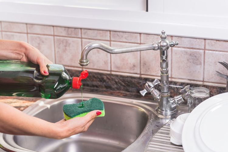 Cropped hand of woman pouring liquid on cleaning sponge in kitchen