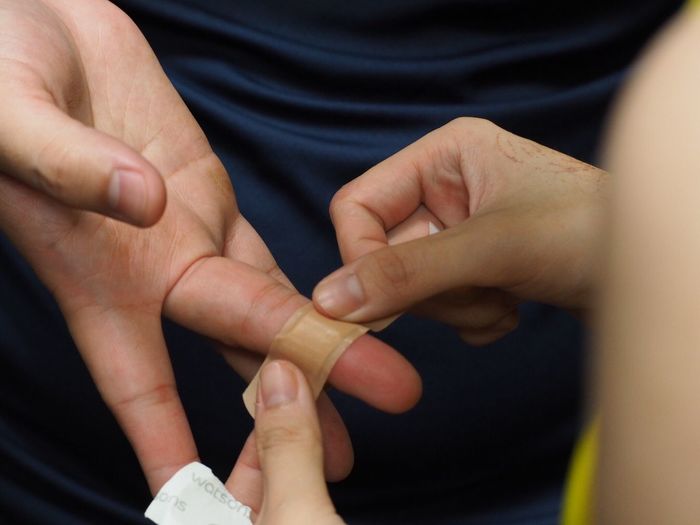 Cropped hand of woman putting adhesive bandage on finger of person