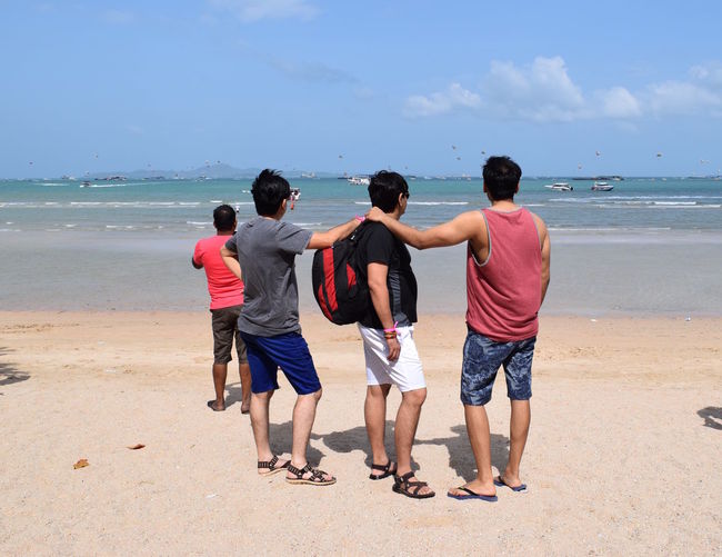 Rear view of friends standing on shore at beach against sky