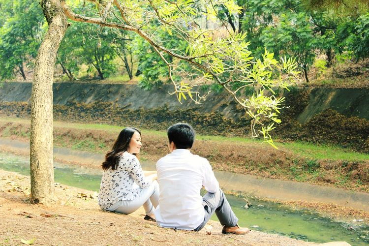 Rear view of couple sitting against trees
