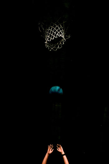 Cropped image of hands throwing basketball into hoop at night