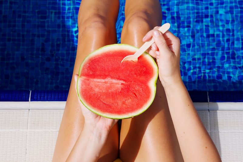 Midsection of woman holding water melon over swimming pool