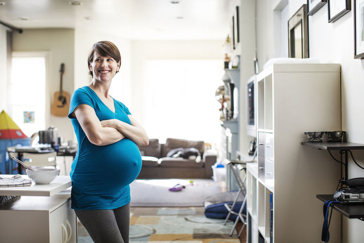 Pregnant woman with arms crossed looking away while standing at home