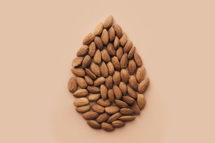 Raw almond kernels drop shape on beige background. cosmetic and healthy food concept, isolated
