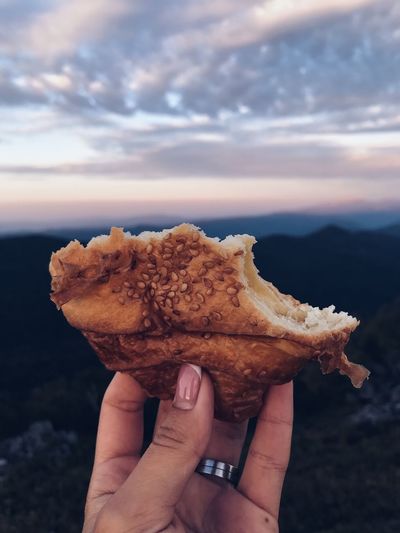 Close-up of hand holding bread against sky