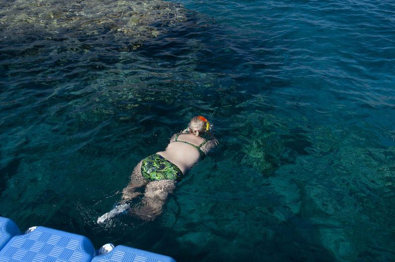 Plump girl in a green swimsuit and a swimming mask, dives and swims in the sea
