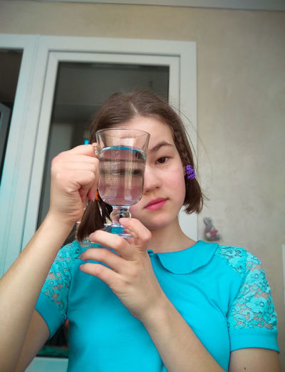 Low angle portrait of girl holding drinking glass against house