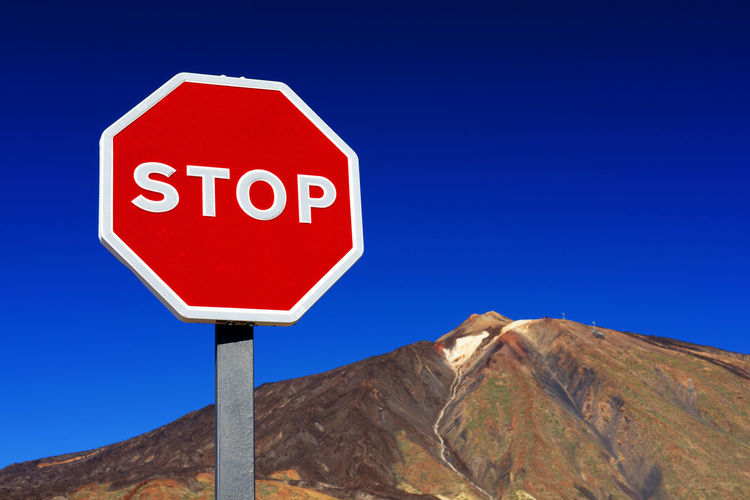 Low angle view of stop sign by rocky mountain at el teide national park against clear blue sky