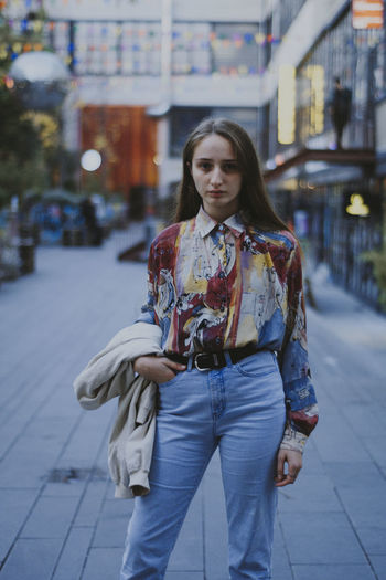 Portrait of young woman standing on footpath in city