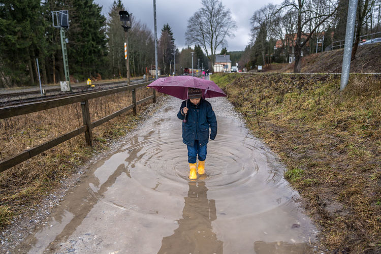 Full length of boy wearing rubber boot walking through puddle during rainy season