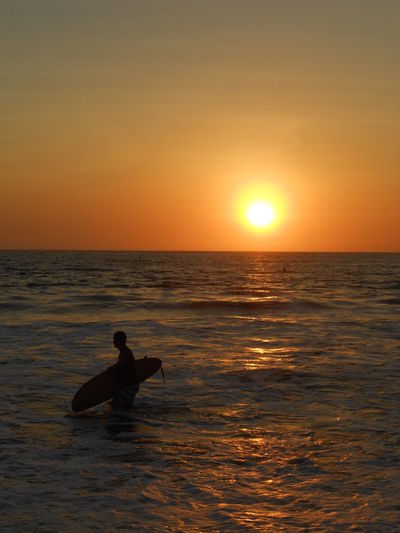 Silhouette person in sea against sky during sunset