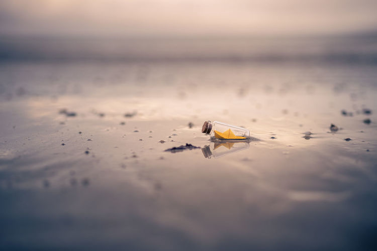 Miniature origami ship in bottle standing on sand at sunrise