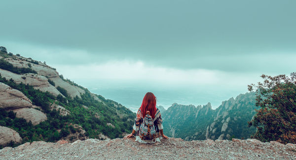 Rear view of female hiker sitting on mountain against sky