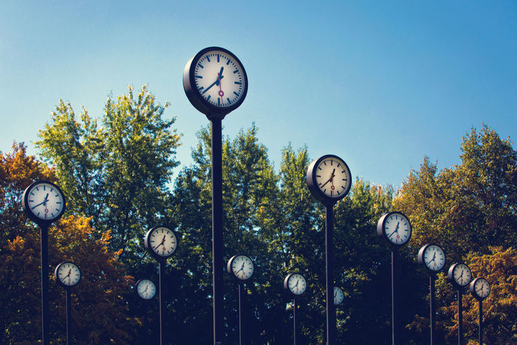 Low angle view of clocks and trees against clear sky