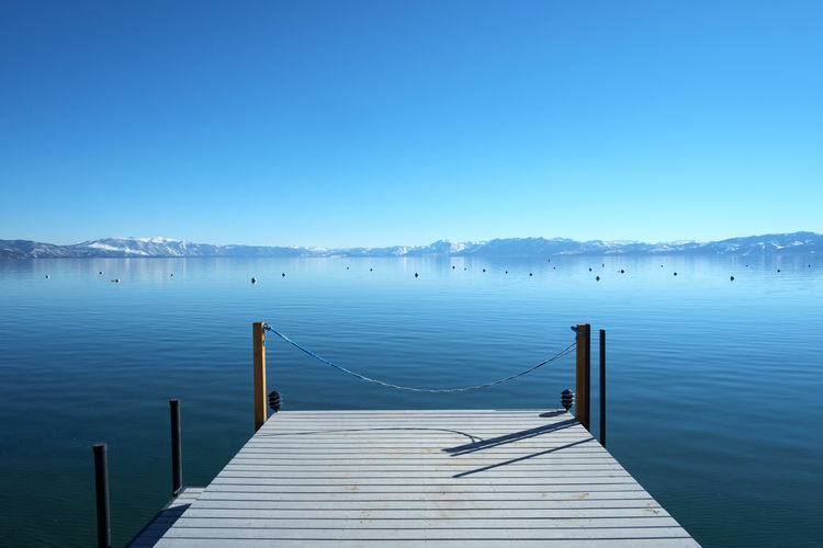 Pier over lake against clear blue sky
