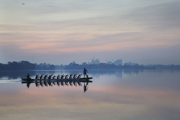 People rowing on lake against during sunrise